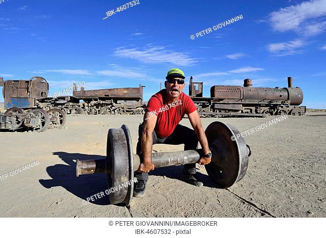 Tourist uses axle as barbell, railway cemetery, Uyuni, Potosi, Bolivia