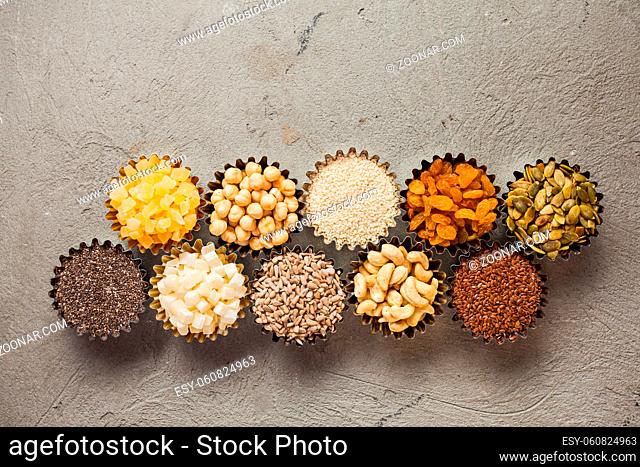 Different nuts and dry fruits in bowls on grey backgound, top view