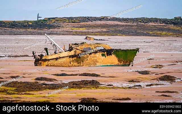 A damaged boat in the mud of the Walney Channel, seen from the road to Roa Island, Cumbria, England, UK