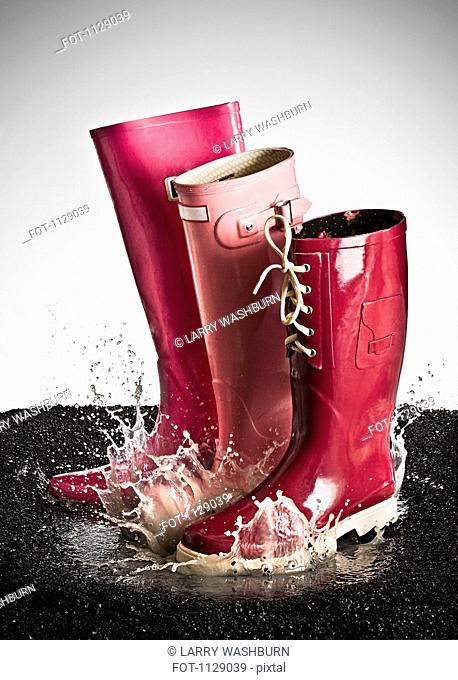 Three pink rubber boots splashing in a puddle