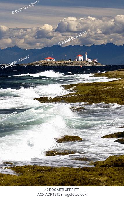 The lighthouse on Entrance Island stands out against a mountainous west coast backdrop amid a crashing surf onto Gabriola Island, Southern Gulf Islands