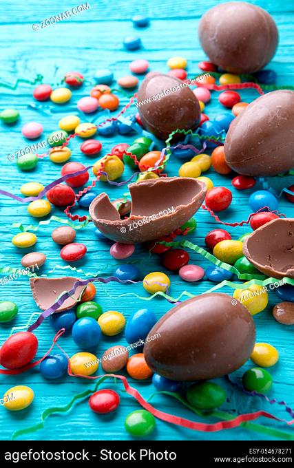 Photo halves of chocolate eggs, colorful chocolates, on blue wooden table
