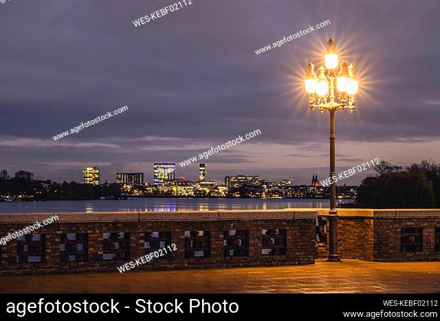 Germany, Hamburg, City skyline seen from Krugkoppelbrucke bridge at night with street light glowing in foreground
