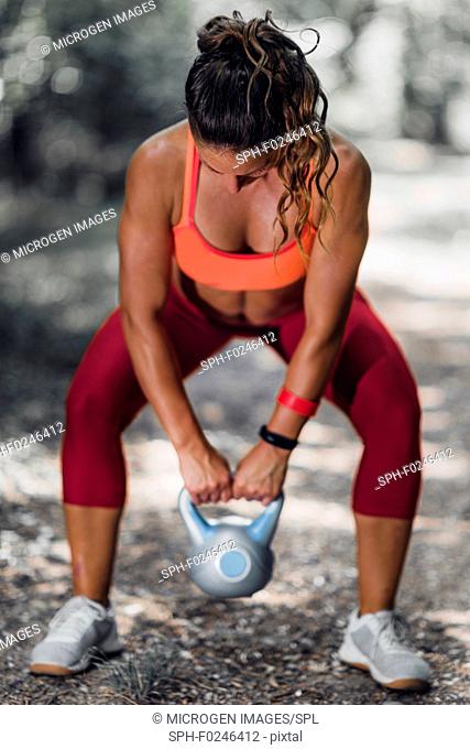 Outdoor exercising. Female athlete exercising with kettlebell in the park