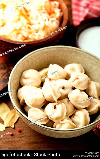Traditional Russian pelmeni dumplings with sour cream and sauerkraut with sour cream over wooden background