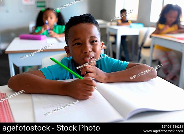 African american elementary schoolboy making face while sitting at desk during class