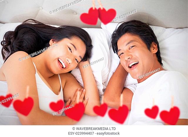 Hearts hanging on a line against happy couple lying in bed smiling at camera