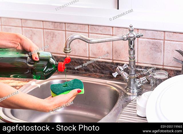 woman with red manicure putting detergent in the scourer, to wash the dishes