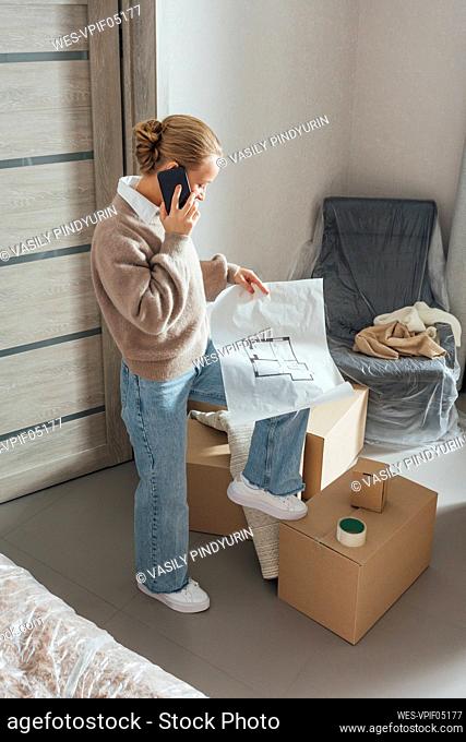Mujer con blueprint hablando por teléfono móvil en un apartamento nuevo
