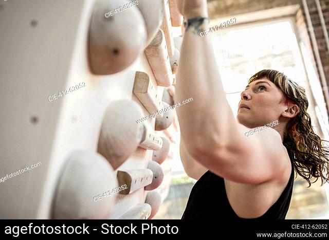 Determined young woman hanging from training board at climbing gym