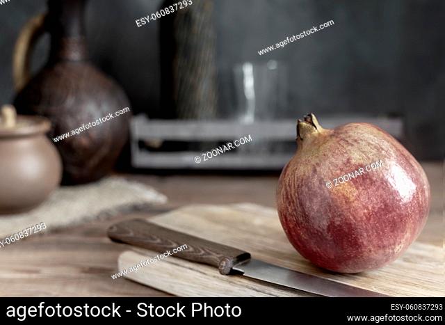 On the kitchen table on the cutting Board is a large ripe pomegranate fruit. Next to it is a kitchen knife. A dark background and copy space