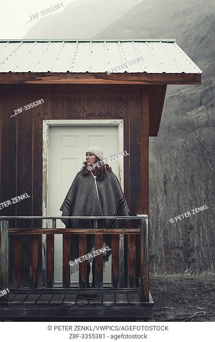 An attractive Woman with stands in front of her cabin and lets her eyes wander across the cold surroundings. Yukon Territory, Canada