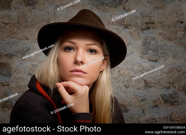 Portraitaufnahme einer jungen Frau mit blonden Haaren und braunem Lodenhut welche nachdenklich zum Betrachter blickt