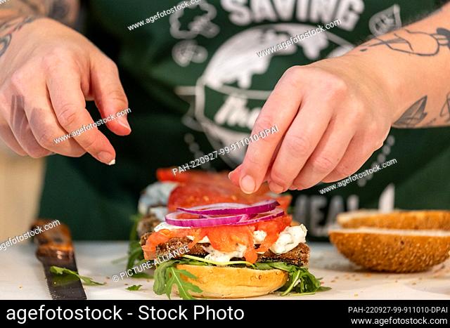 PRODUCTION - 27 July 2022, Bavaria, Nuremberg: A cook occupies at the fair Biofach during a cooking show to vegan fish substitute burger with onions