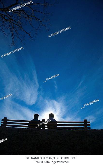 Women talking under whispy clouds while sitting on park bench