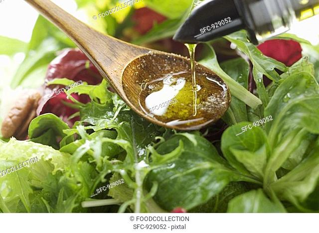 Pouring olive oil into wooden spoon above salad leaves
