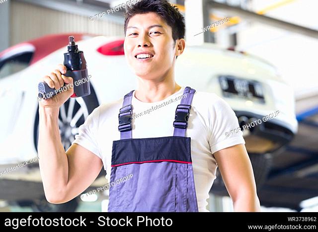 Asian Chinese car mechanic with tool in front of luxury car in auto workshop