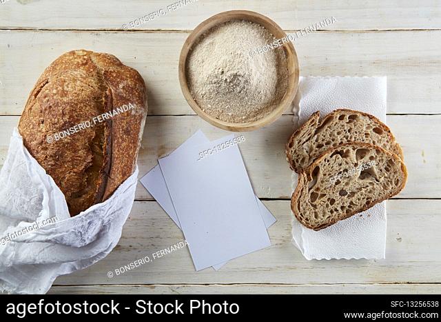 Wooden table with one sourdogh bread, two slices of bread and some flour