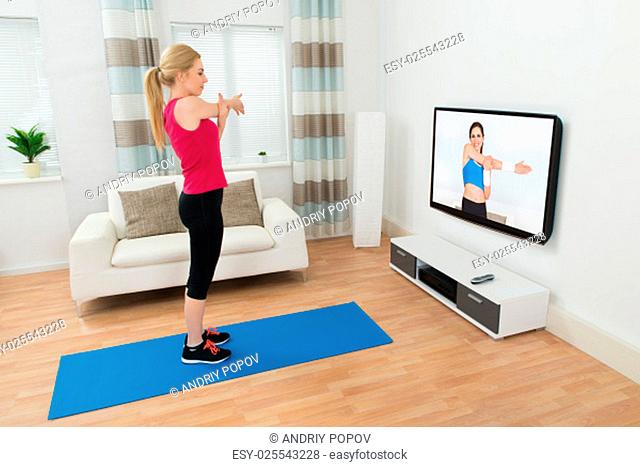 Young Woman Exercising In Front Of Television In Living Room