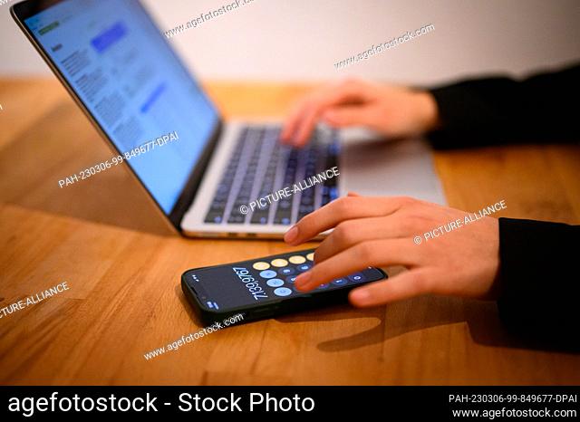 PRODUCTION - 12 February 2023, Hamburg: A woman sits at her laptop with calculator app on her phone (posed scene). Photo: Jonas Walzberg/dpa