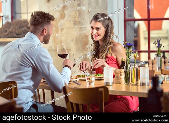 Happy young couple eating food with red wine at restaurant