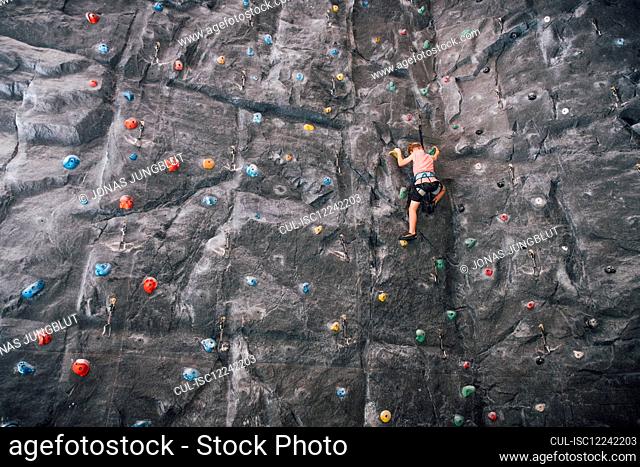 Low angle view of young boy ascending rock climbing wall in Bolzano, Lombardy, Italy