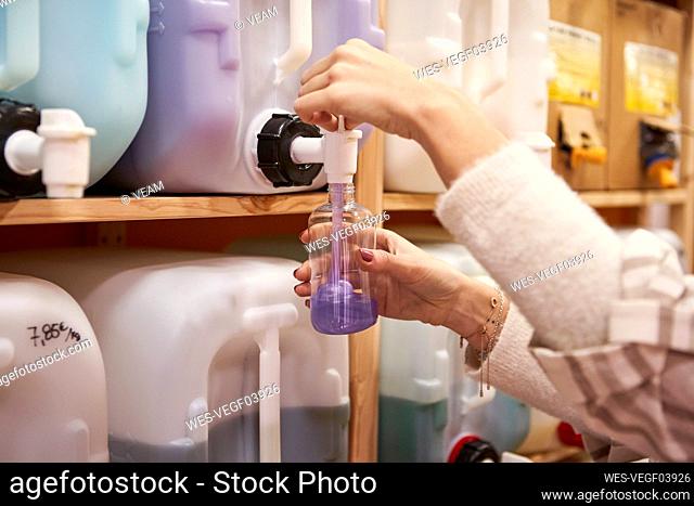 Woman filling purple liquid in bottle from cane at store