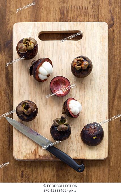 Mangosteens on a wooden chopping board with a knife