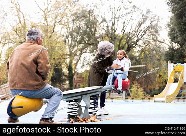 Grandparents playing with granddaughter on seesaw at playground