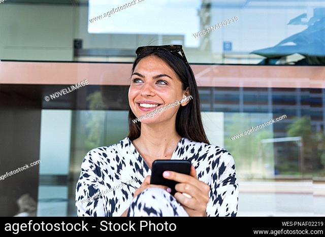 Smiling young woman listening music in front of glass