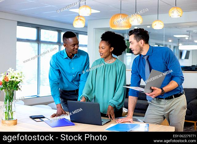 Happy diverse business people using laptop and discussing in modern office