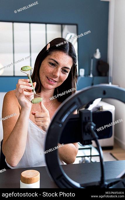 Smiling woman showing jade stone roller on smart phone at home
