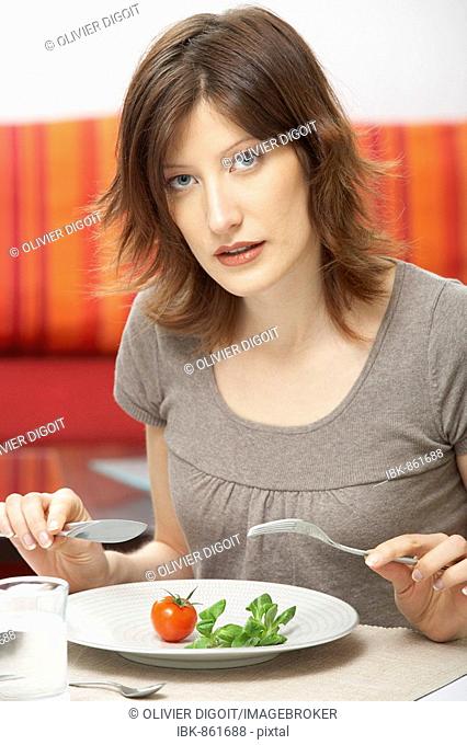 Young woman with a single tomato and piece of lettuce on her plate