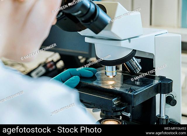 Young woman analyzing human brain microscope slide under microscope while sitting at laboratory