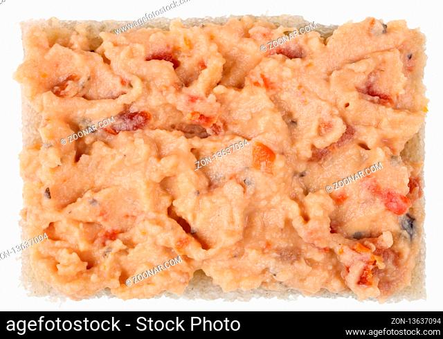 A rectangular piece of gray rye bread is smeared with hummus paste (mutton or chick peas) with paprika and onions. Isolated on white studio macro food shot