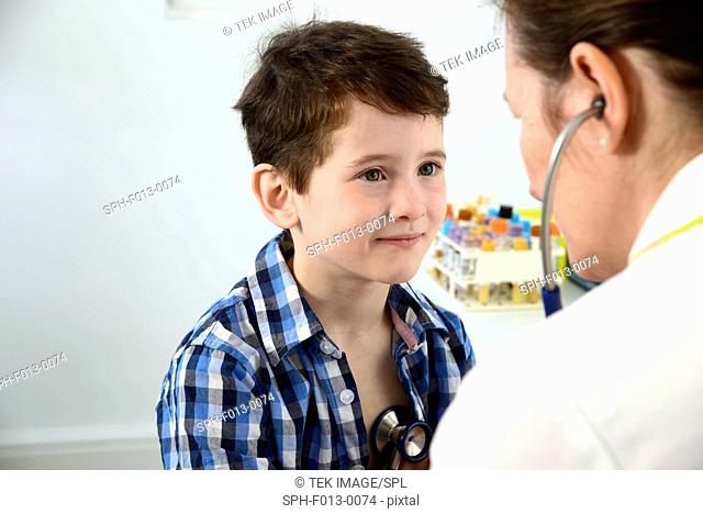 General practice doctor presses a stethoscope onto the chest of a young boy