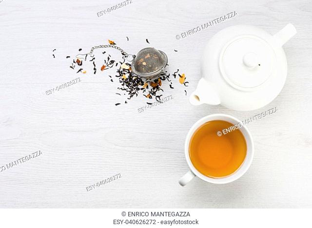 cup of tea with teapot and closed infuser with black tea on table
