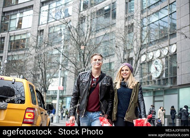 Smiling couple carrying shopping bags while walking on street in city