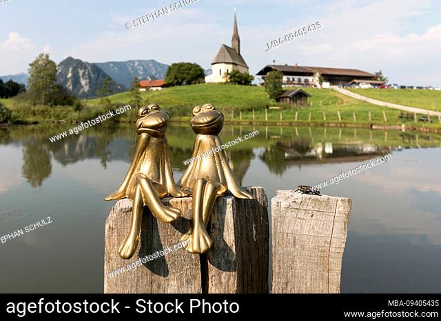 Germany, Bavaria, Inzell, brass frogs with a large fly, St. Nicholas Church in the Bavarian community of Inzell, district Einsiedl, in the background, Alps