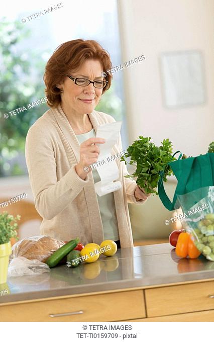 Senior woman reading shopping list in kitchen