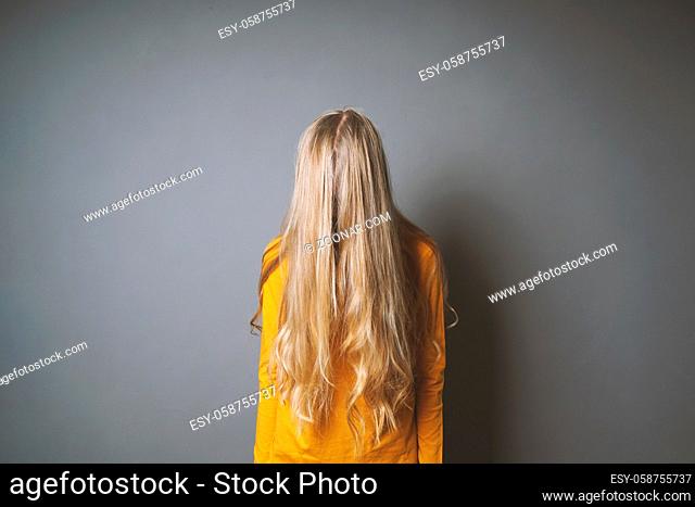 depressed young woman hiding her face behind long blond hair - shy or indifferent teenage girl