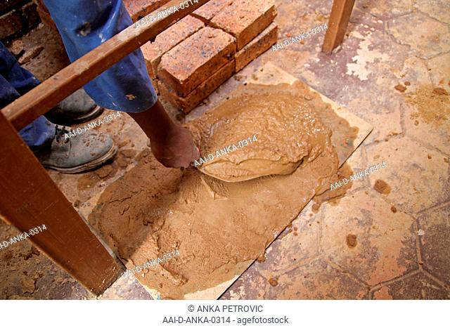Brick layer laying bricks, picking up concrete cement mixture from ground, Moreleta Park, Pretoria, Gauteng Province, South Africa