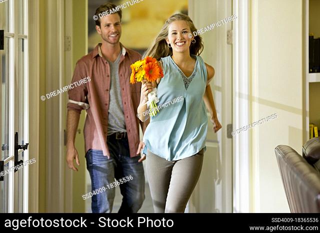 Young woman running through home past wall of windows holding a bouquet of flowers