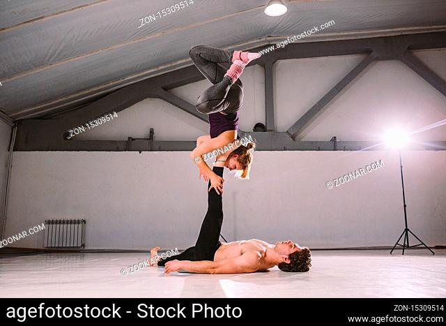 Theme sport and a healthy lifestyle. Acrobatics and acroyoga. Young sporty couple practicing acroyoga handstand. Male and female acrobats doing together Acro...