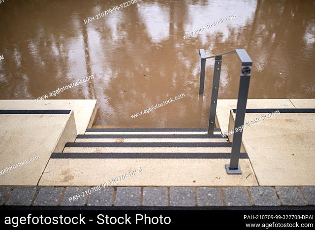 09 July 2021, Bavaria, Herzogenaurach: Steps of a seating area at the river Aurach, which has risen over its banks due to continuous rainfalls, are under water