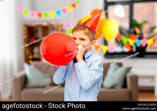 little boy in birthday party hat blowing balloon