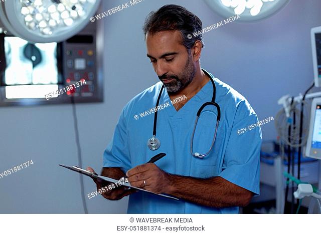 Mature male surgeon writing on clipboard in operation room at hospital