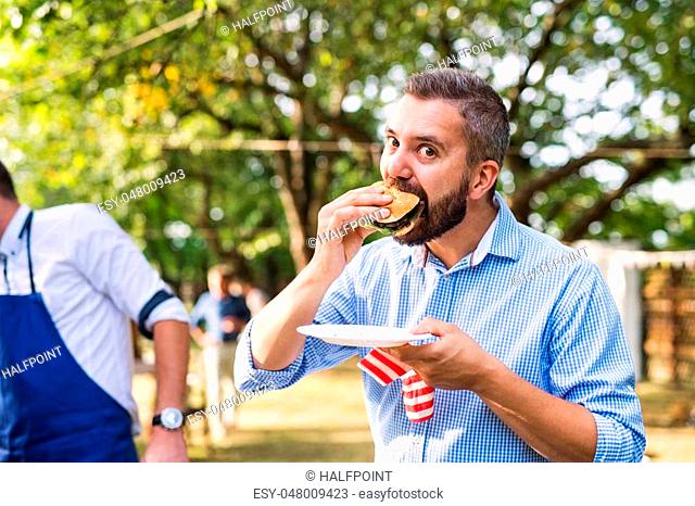 Family celebration outside in the backyard. Barbecue party. A mature man eating hamburger