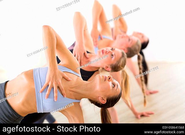 Group of young sporty attractive women in yoga studio, practicing yoga lesson with instructor, forming a line in Trikanasana asana pose