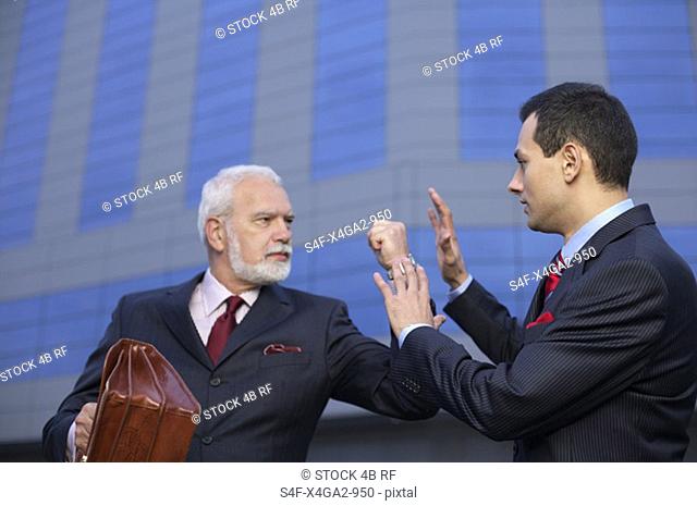 Mature businessman with fist up, an other businessman holding hands up